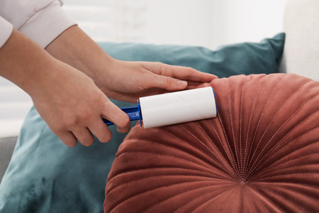 Woman cleaning cushion with lint roller at home, closeup