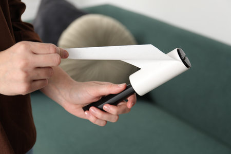 Woman removing sticky tape from lint roller at home, closeup