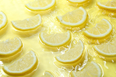 Slices of lemon in water on yellow background, closeupの写真素材