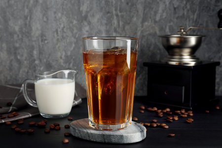 Iced coffee, milk, grinder and beans on black wooden table