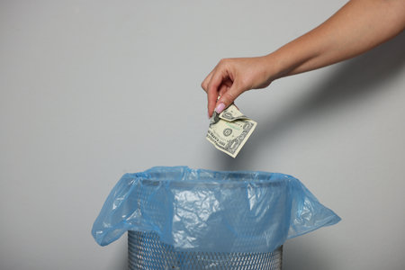 Woman throwing dollar banknotes into trash bin near light wall indoors, closeupの写真素材