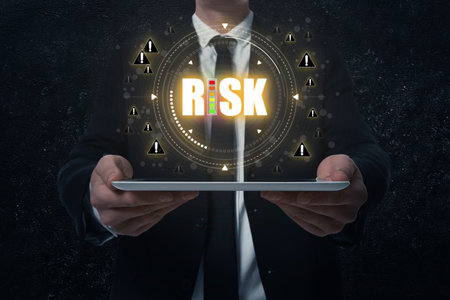 Businessman holding tablet computer against black background, closeup. Word Risk surrounded by warning signs above deviceの写真素材