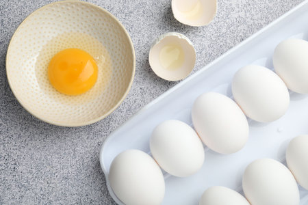 whole Many raw chicken eggs and broken one in bowl on gray table, flat lay