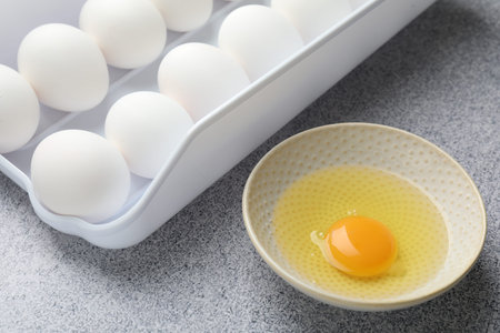 Many raw chicken eggs and broken one in bowl on gray table, closeup