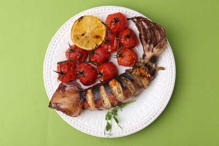 Tasty stuffed squid, microgreens, lemon and tomatoes on green background, top view