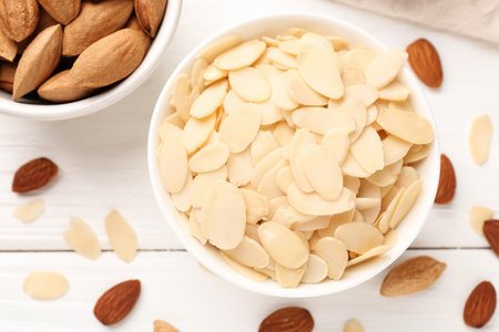 Fresh almond flakes and whole nuts on white wooden table, flat layの写真素材