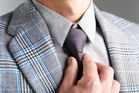 Man in suit adjusting his necktie on gray background, closeupの写真素材
