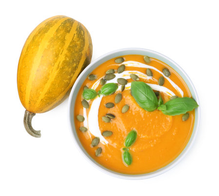 Delicious pumpkin soup with seeds in bowl, basil and vegetable isolated on white, top viewの写真素材