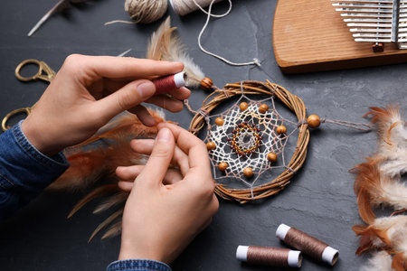 Woman making beautiful dream catcher at dark textured table, closeupの写真素材