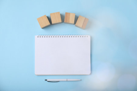 Blank wooden cubes, notebook and pen on light blue background, flat lay. Bokeh effectの写真素材