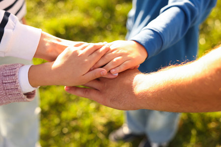 Parents and their children holding hands outdoors, closeup. Family bonding