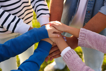 Parents and their children holding hands outdoors, closeup. Family bonding