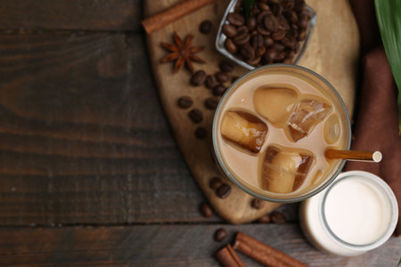 Iced coffee in glass, milk and beans on wooden table, flat lay. Space for text