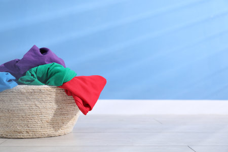 Laundry basket full of clothes on floor near light blue wall, space for textの写真素材