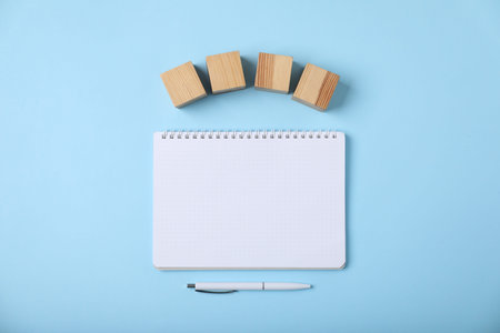 Blank wooden cubes, notebook and pen on light blue background, flat lay