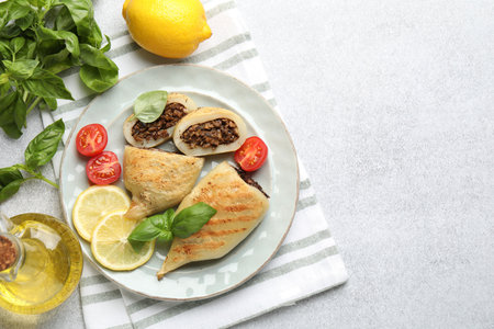 Pieces of tasty grilled squid stuffed with mushrooms, basil, tomatoes and lemon on light gray...