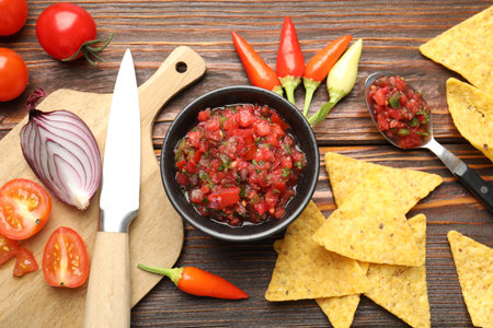Tasty salsa sauce with nachos, knife and ingredients on wooden table, flat layの写真素材