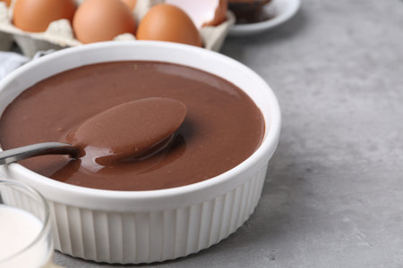 Liquid chocolate dough in bowl and ingredients on gray table, closeup. Space for textの写真素材