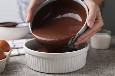Woman pouring raw chocolate dough into baking dish at gray table, closeupの写真素材