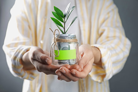 Woman holding jar with blank note, money and sprout on gray background, closeupの写真素材