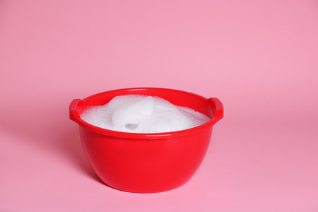 Red plastic basin with soapy water on pink backgroundの写真素材