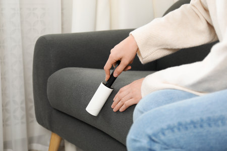 Woman cleaning sofa with lint roller at home, closeupの写真素材