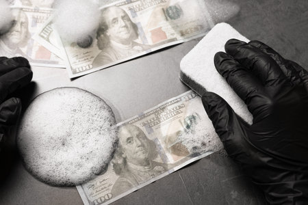 Money laundering. Man washing dollar banknotes with sponge and foam at black table, top viewの写真素材