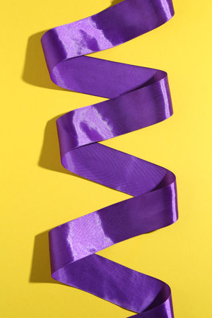 Beautiful violet ribbon on yellow background, top viewの写真素材