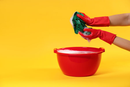 Woman washing clothes in plastic basin on yellow background, closeup. Space for textの写真素材