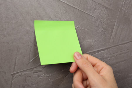 Woman putting blank adhesive note onto gray wall, closeup. Space for textの写真素材