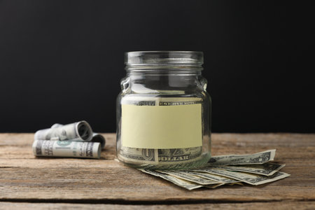 Jar with blank note and money on wooden table against black backgroundの写真素材