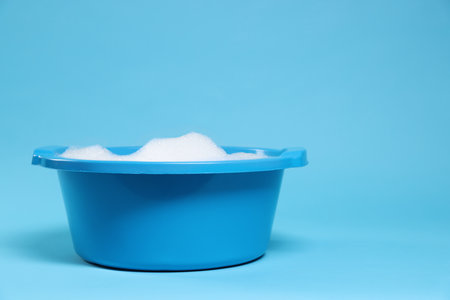 Plastic basin with soapy water on light blue background. Space for textの写真素材