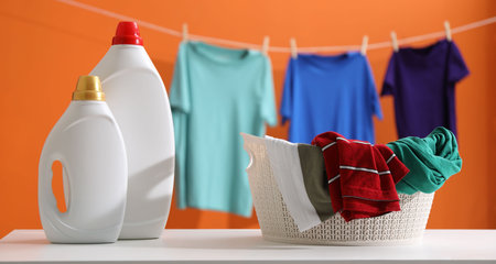 Bottles of fabric softener and clothes on white table and hanging garment against orange backgroundの写真素材