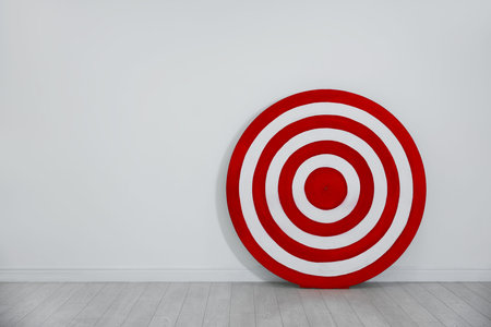 Round shooting target on floor near white wall, space for text