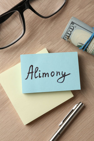 Notes with word Alimony, money, pen and glasses on wooden table, flat layの写真素材