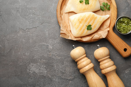Salt, pepper mills, pieces of grilled squid, parsley and sauce on gray textured table, flat lay. Space for textの写真素材