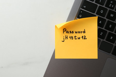 Paper note with password and laptop on white marble table, top view. Space for textの写真素材