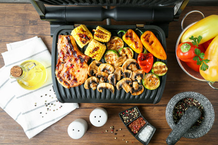 Electric grill with steak and vegetables on wooden table in kitchen, flat layの写真素材