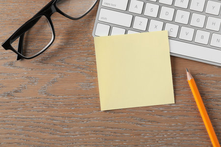 Blank note, glasses, keyboard and pencil on wooden table, flat lay. Space for textの写真素材