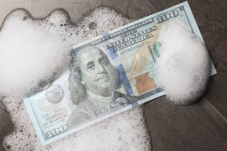 Money laundering. Dollar banknote and foam on black table, top viewの写真素材