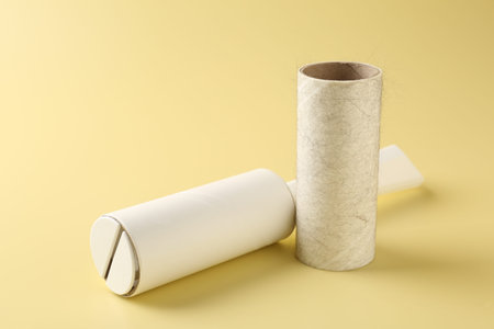 Lint roller and used adhesive roll on yellow background, closeup