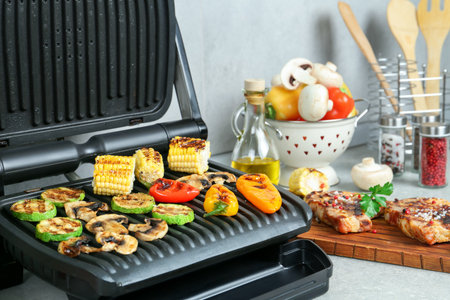 Electric grill with delicious vegetables and steaks on light table in kitchen, selective focusの写真素材
