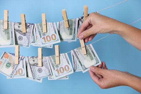 Money laundering. Banknote on clothesline against light hanging blue background, closeupの写真素材