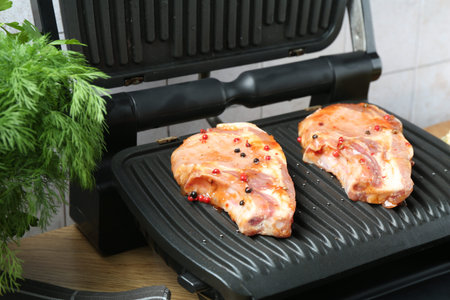 Electric grill with uncooked steaks and herbs on wooden table, closeupの写真素材