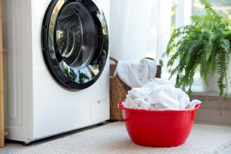 Plastic basin with laundry near washing machine in bathroomの写真素材