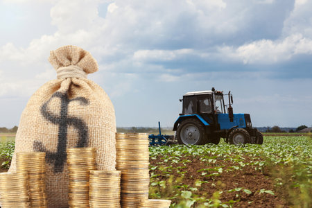 Bag with dollar sign and coins against tractor in fieldの写真素材