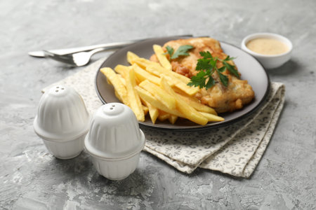 Salt, pepper shakers, sauce, British traditional fish and chips on gray textured table, closeup