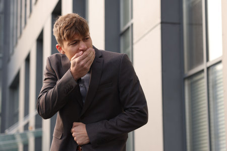 Young man in suit suffering from stomach ache and nausea outdoorsの写真素材