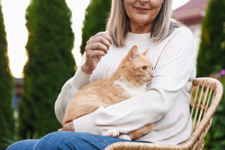 Senior woman with her cute cat in wicker armchair outdoors, closeupの写真素材