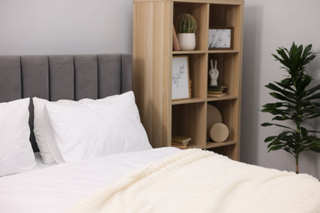 Large bed with linens, houseplant and shelving unit near gray wall in bedroomの写真素材